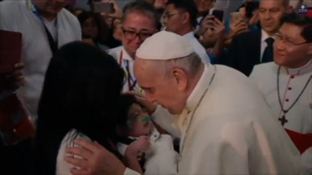 Pope Francis prays for a sick infant with an oxygen tube at the Mall of Asia Arena.