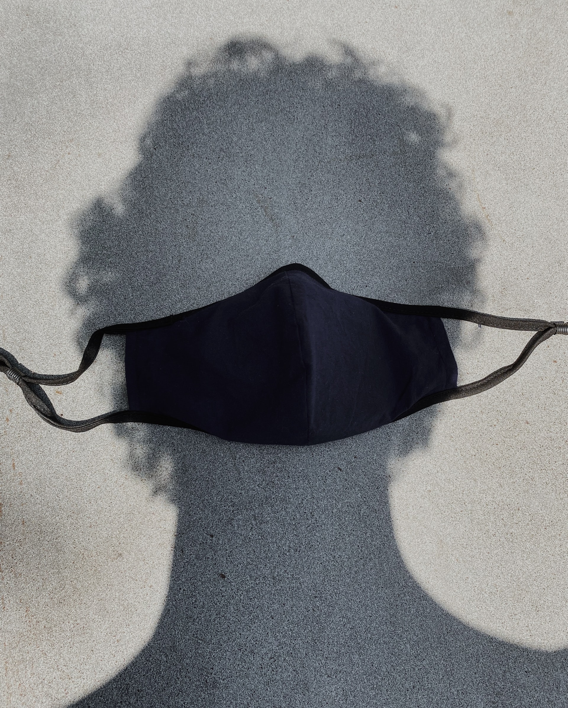 A black mask on a person's head's shadow on a gray background
