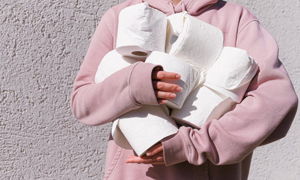 Woman in hoodie holding toilet paper rolls
