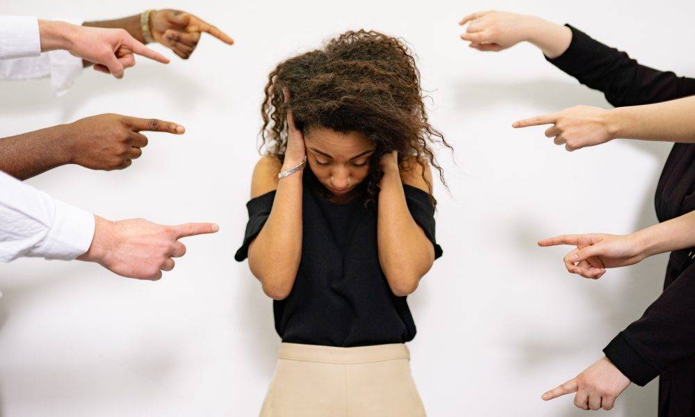 Fingers pointing at a woman who is covering her ears