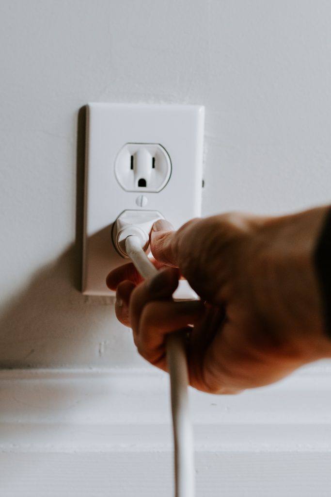 Hand plugging a white cord into an outlet
