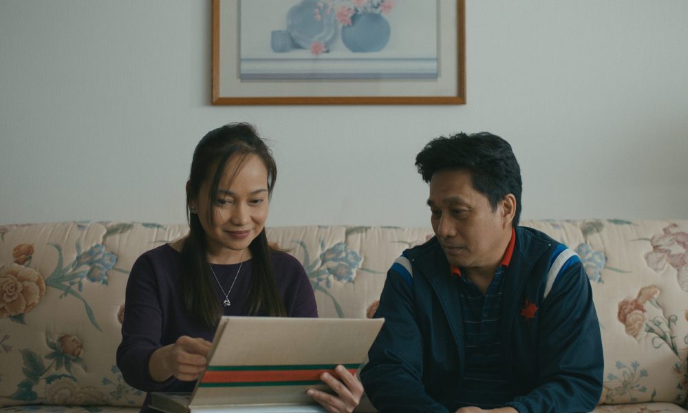 A film still from Islands of two people on a living room sofa looking through an album of old family photographs