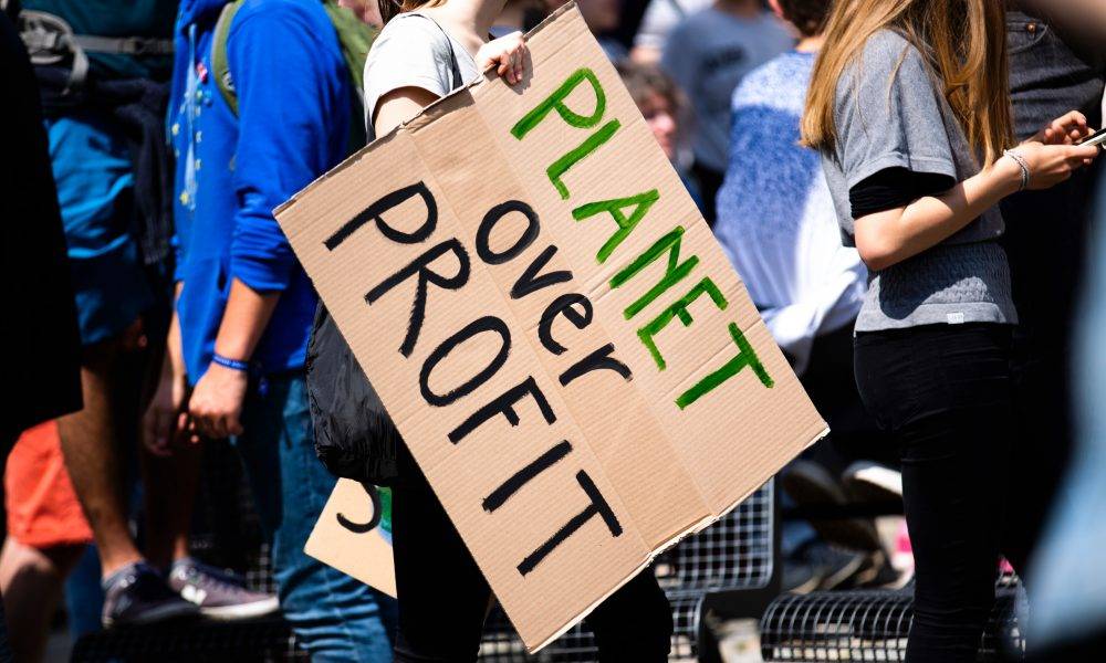 Woman holding Planet over Profit placard