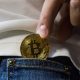 person putting gold bitcoin in pocket