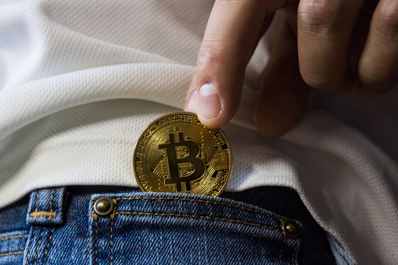 person putting gold bitcoin in pocket