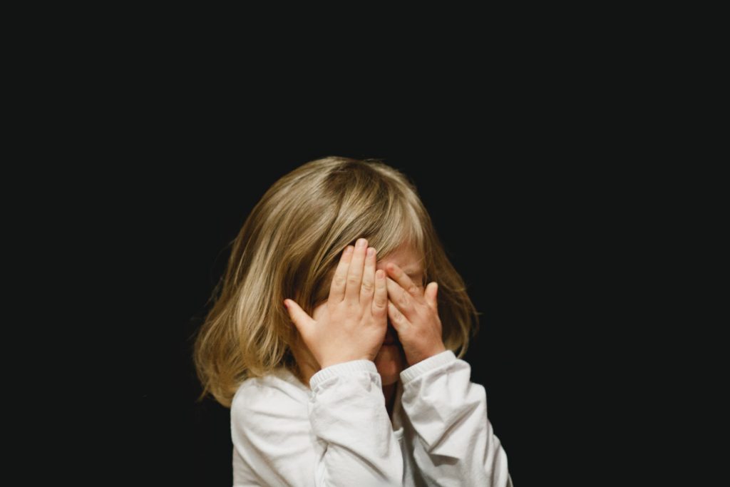 Child covering their face on a black background