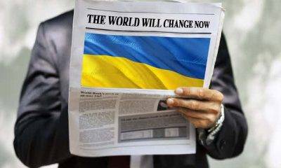 Hand holding newspaper with Ukraine flag and the words "The World Will Change Now"
