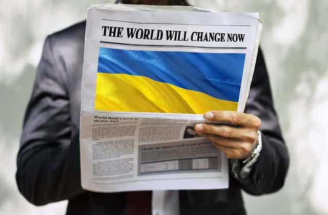 Hand holding newspaper with Ukraine flag and the words "The World Will Change Now"