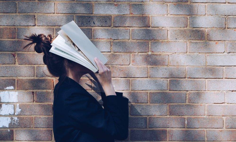 School Girl with Book in front of natural rustic red brick background holding book up to her face