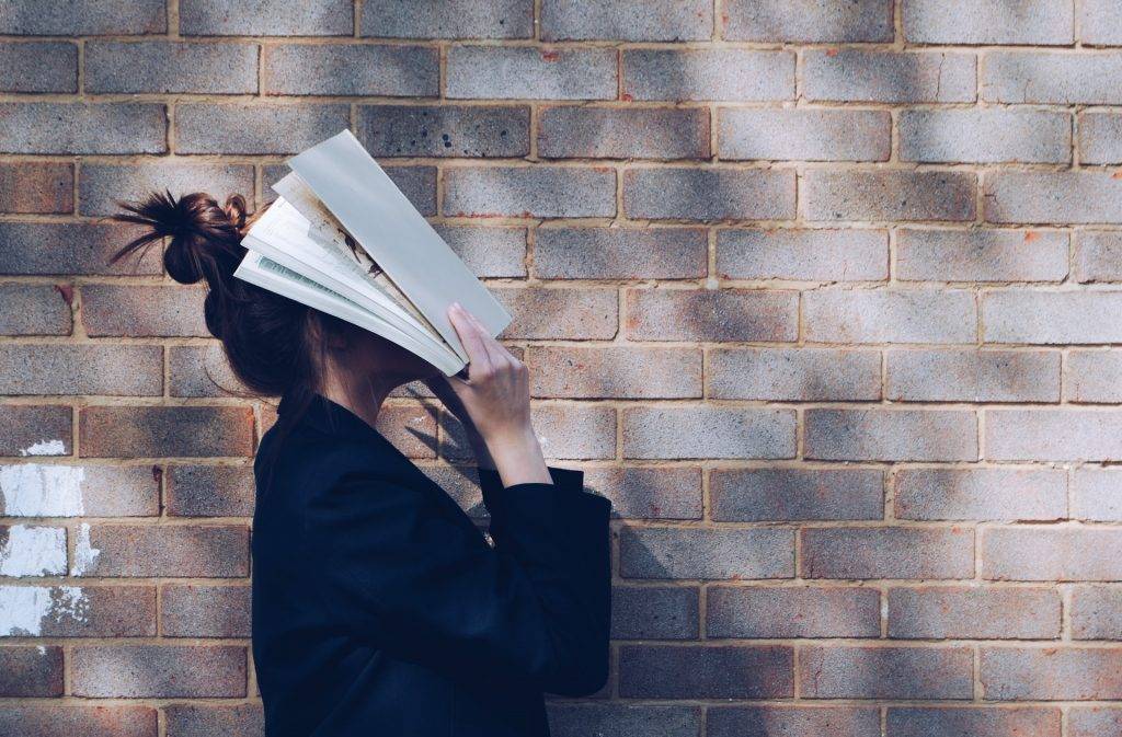 School Girl with Book in front of natural rustic red brick background holding book up to her face