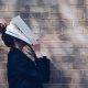 School Girl with Book in front of natural rustic red brick background holding book up to her face