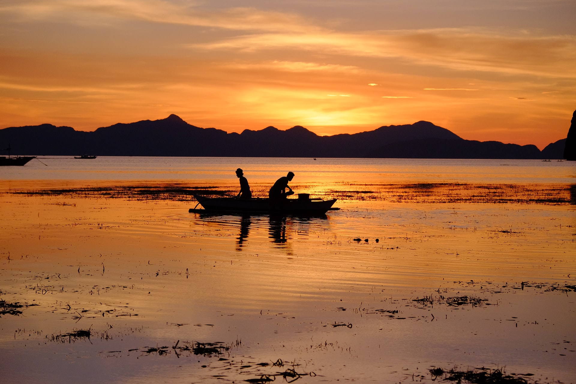 silhouette of two people in a boat in a body of water during sunset