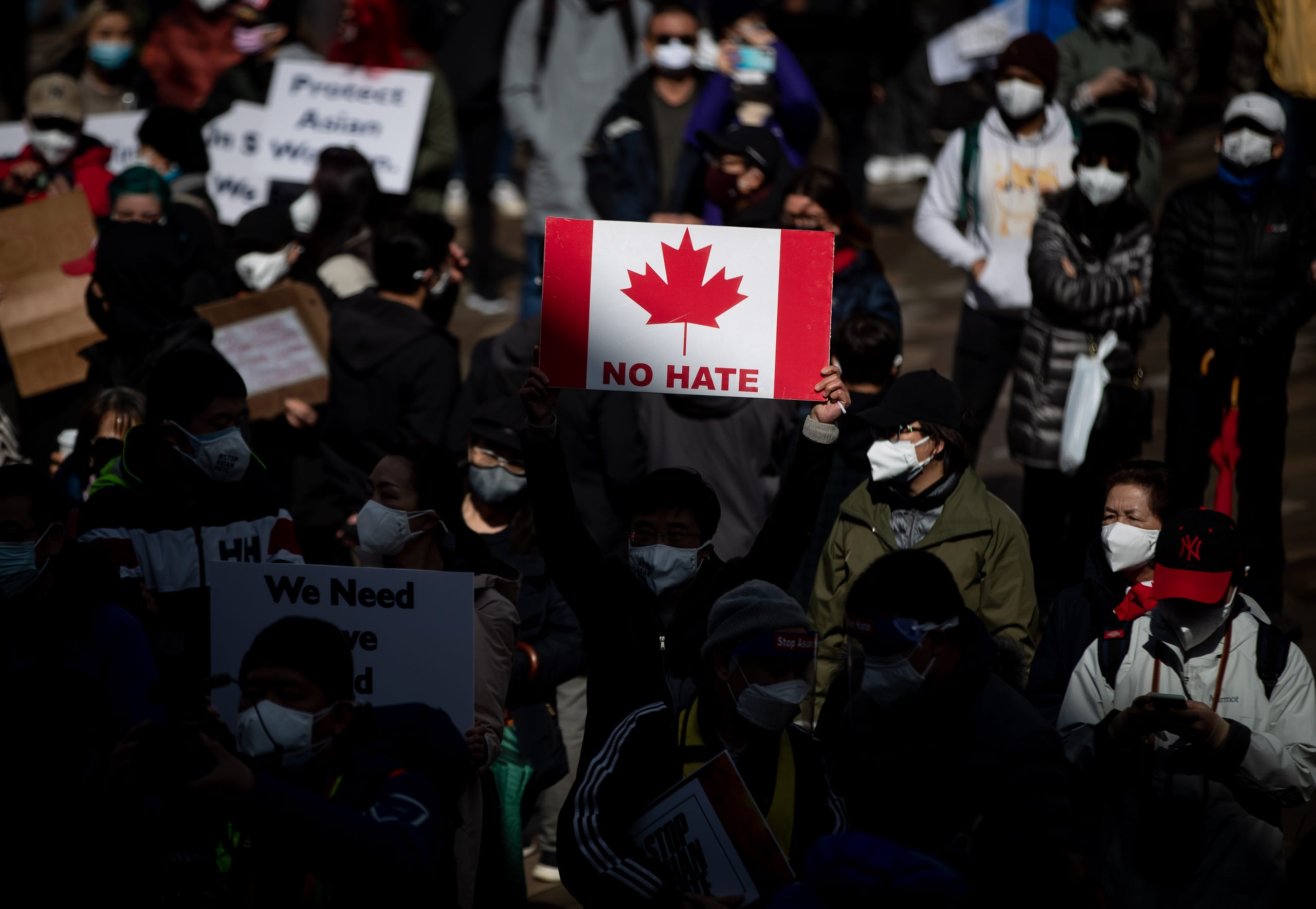 A person holds a Canadian flag sign with the words no hate