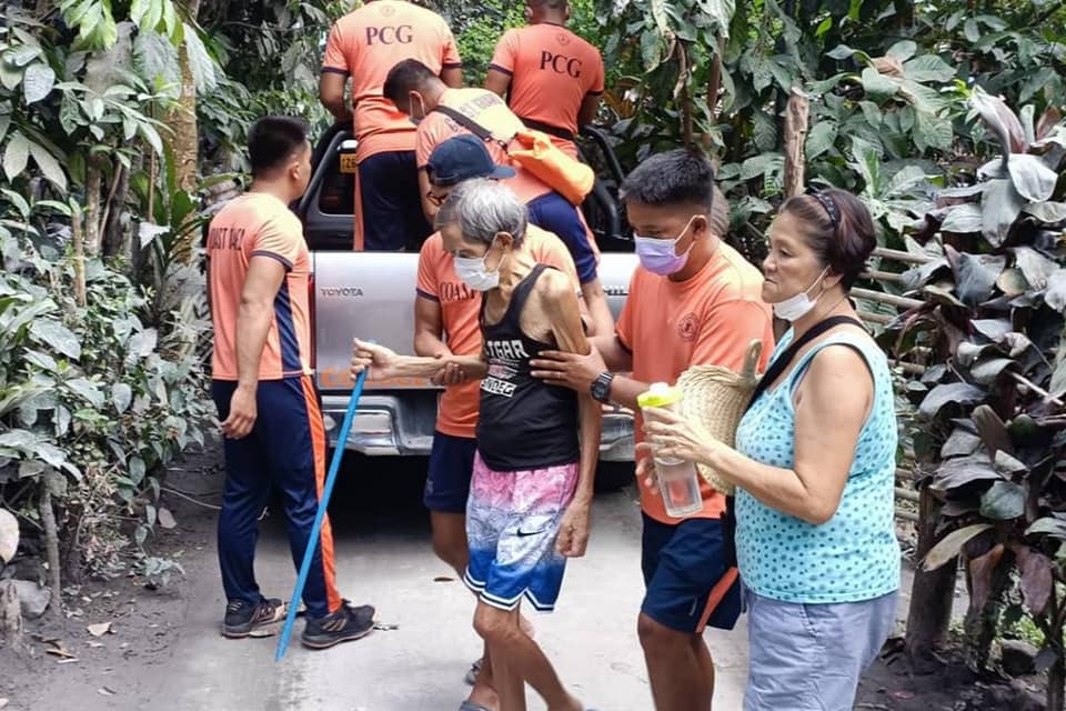 Elderly being assisted by people wearing orange