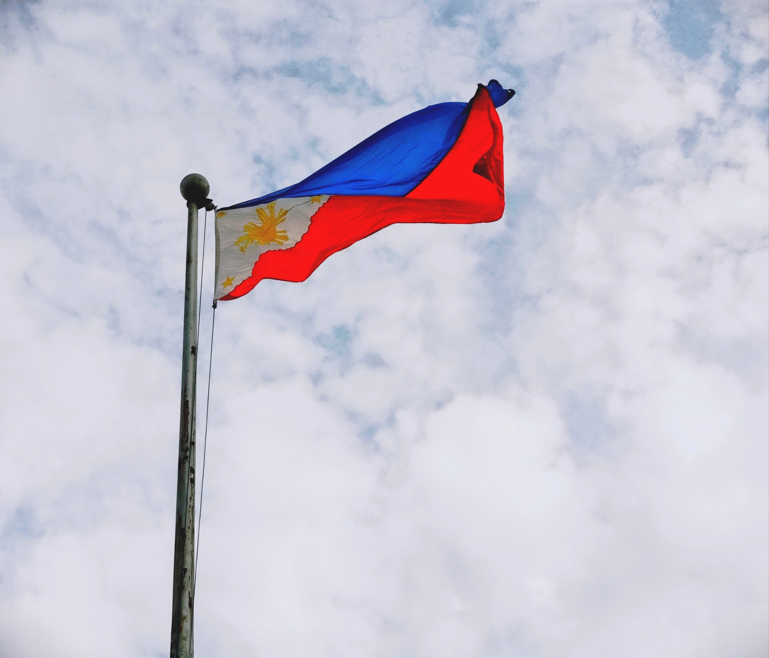 Philippine Flag Swaying by the Wind Under White Sky