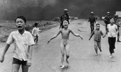 Black and white photo of children running with soldiers walking