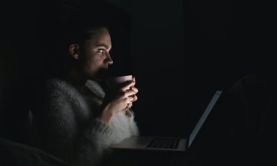 Woman holding a cup in front of laptop in a dark room