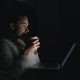 Woman holding a cup in front of laptop in a dark room