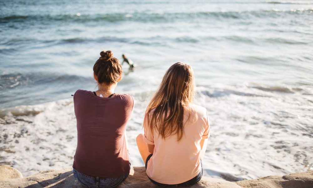 two girls sitting looking at the sea