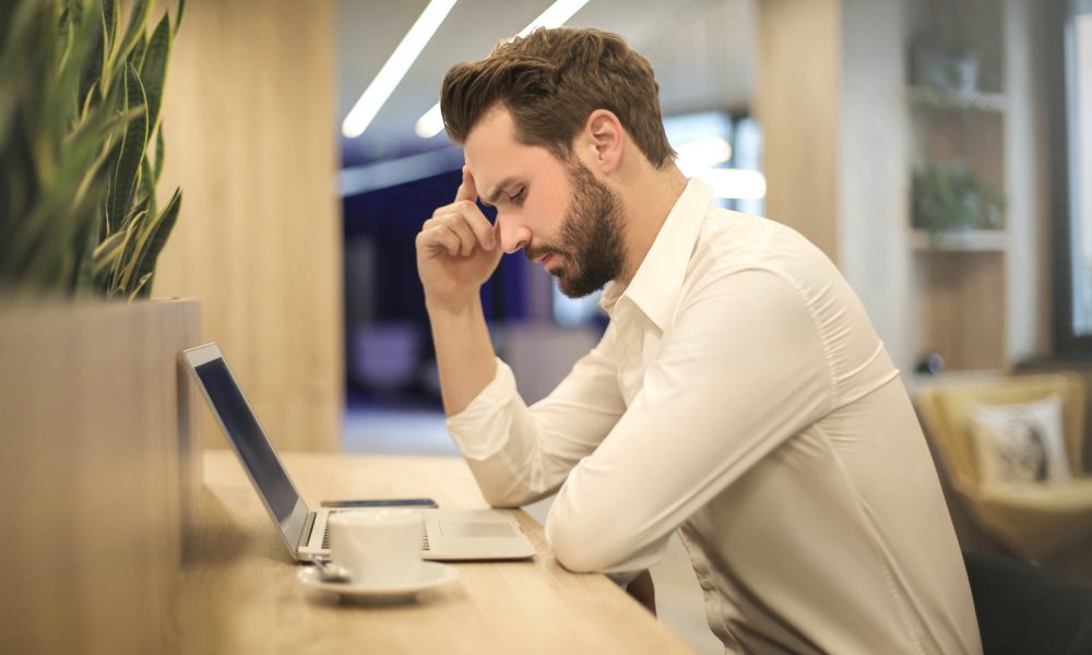 Man With Hand on Temple Looking at Laptop