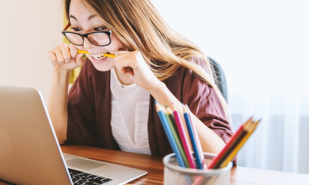 girl biting pencil while looking at laptop screen