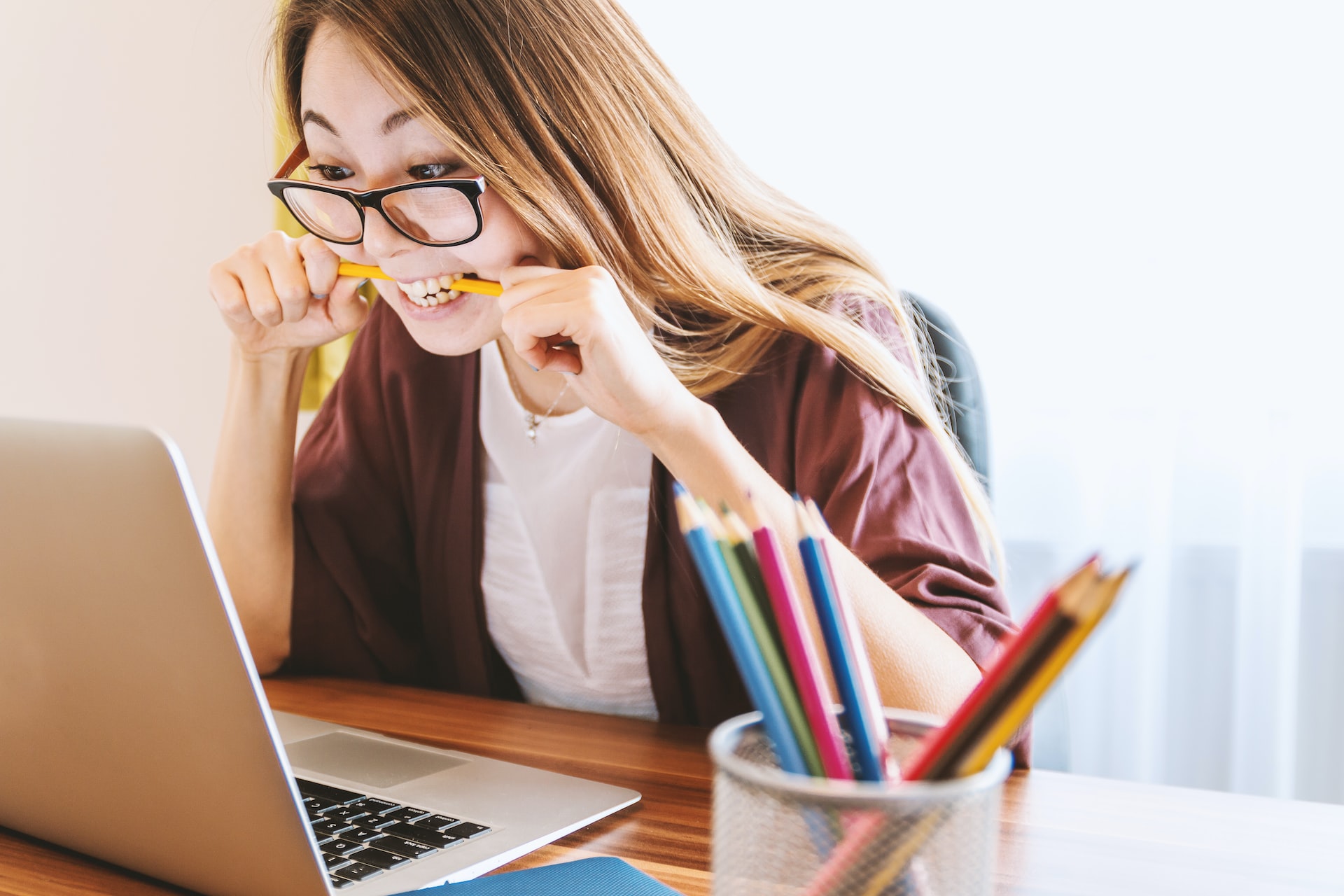 girl biting pencil while looking at laptop screen