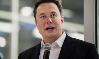 Elon Musk wearing black coat holding mic