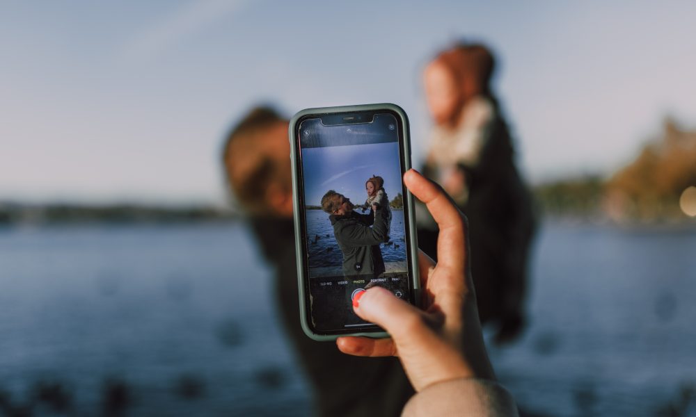 Person Taking Photo of Man Carrying a Baby