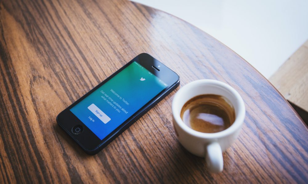 White Ceramic Teacup Beside Black Iphone 5 on Brown Wooden Table