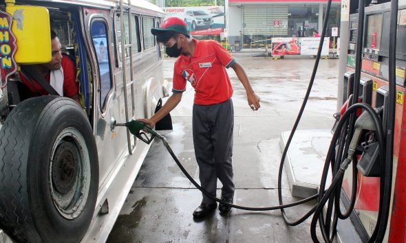 gasoline attendant fills up the fuel tank of a jeepney