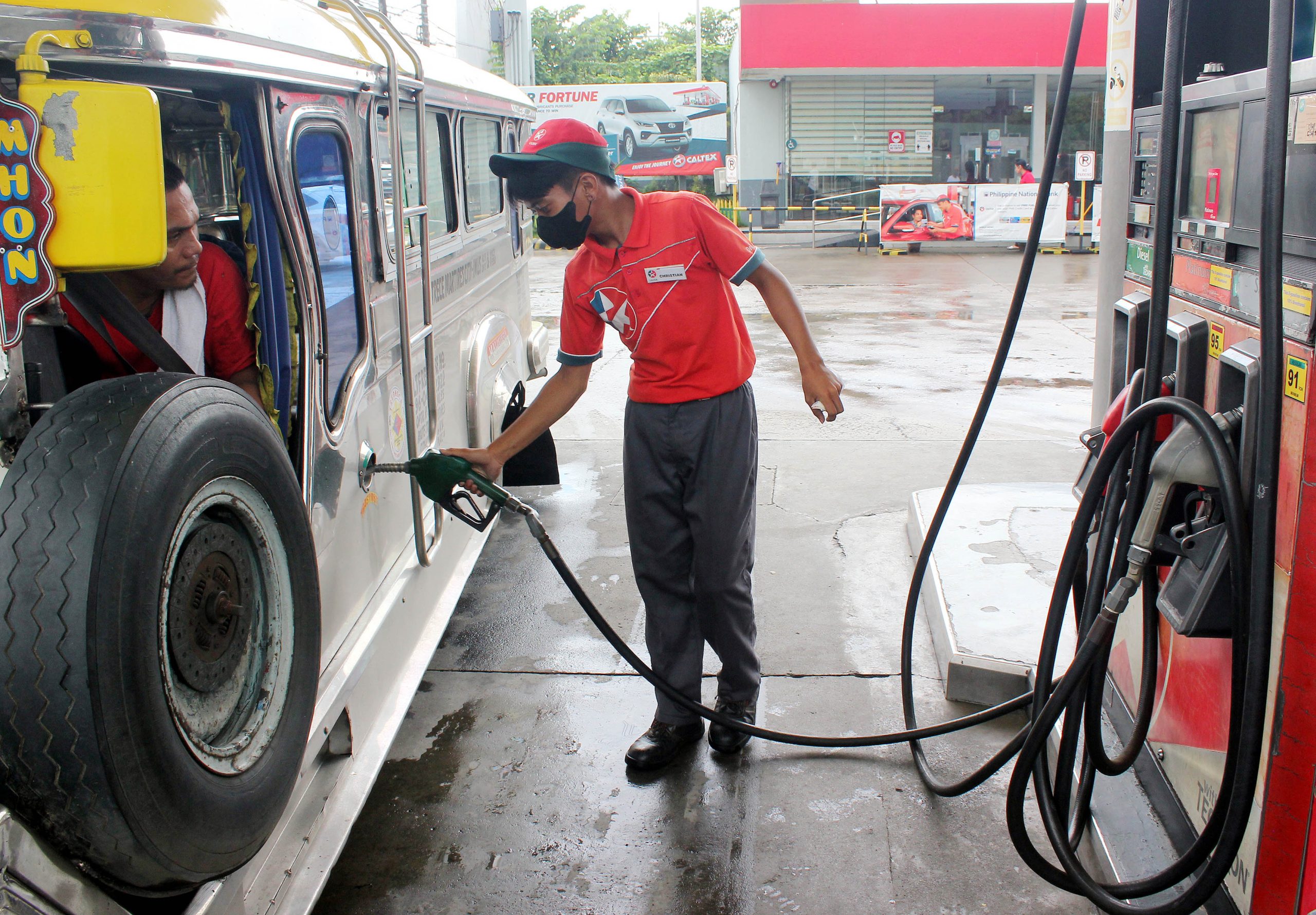 gasoline attendant fills up the fuel tank of a jeepney