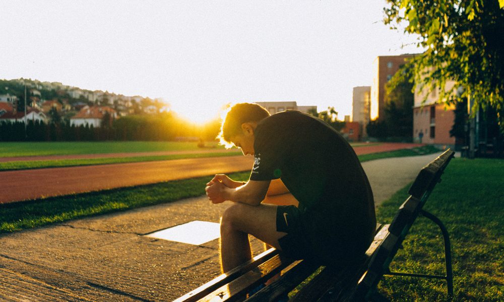 Man Sitting on Bench Near Track Field While Sun Is Setting