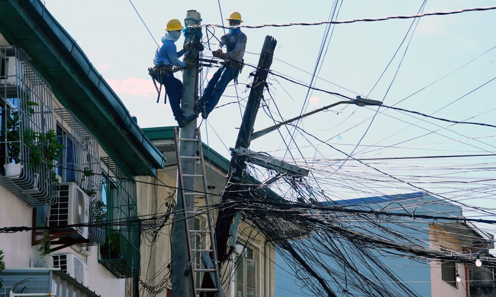 Two linemen disentangle and transfer the wires to a concrete power pole from the leaning power pole