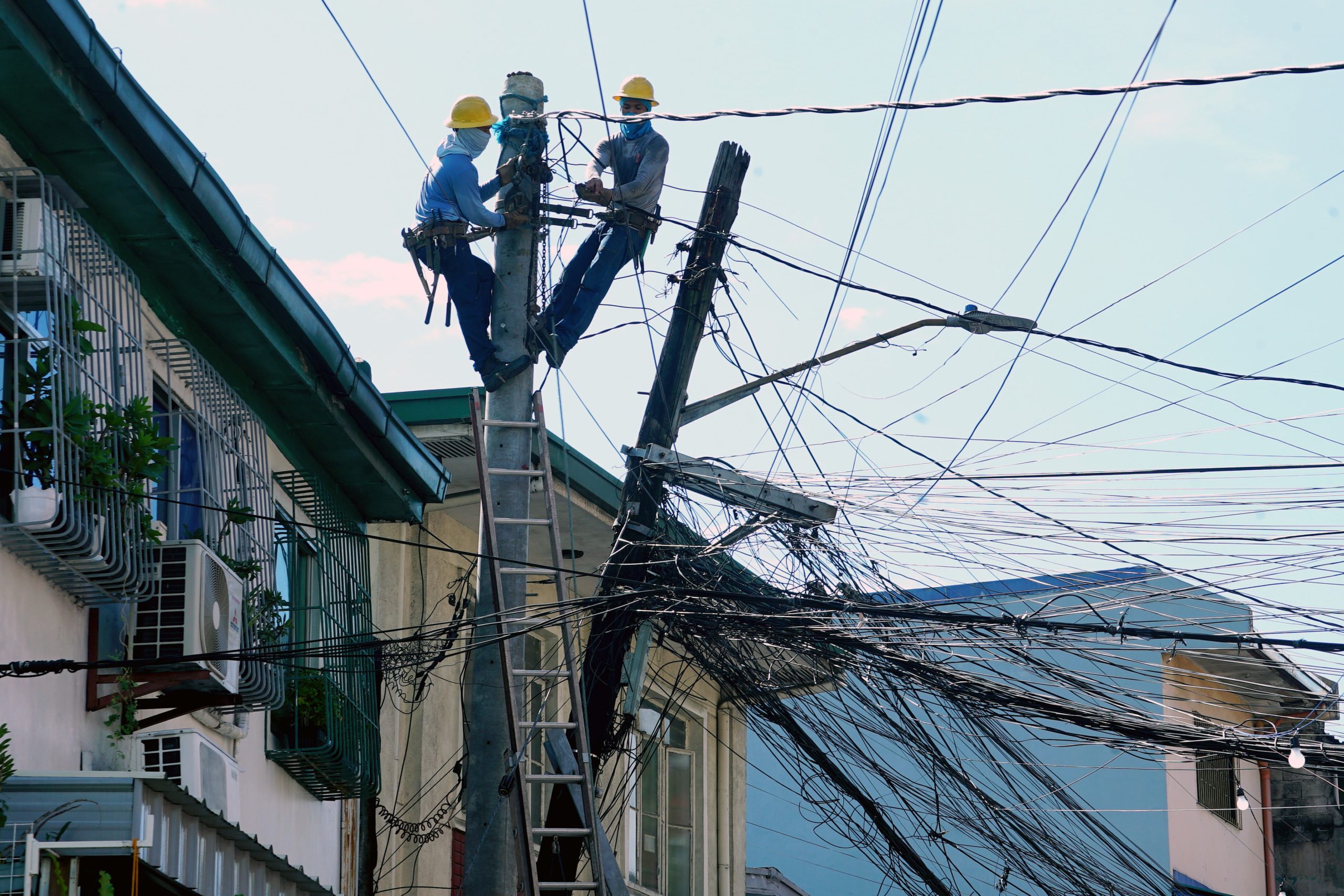 Two linemen disentangle and transfer the wires to a concrete power pole from the leaning power pole