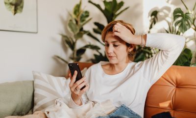 Woman Sitting on Sofa, Looking at Phone and Scratching Her Head