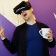 Man Wearing Black Virtual Reality Headset while Holding White Mug