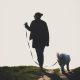 Silhouette Of A Woman Walking Her Dog On Uphill Pathway