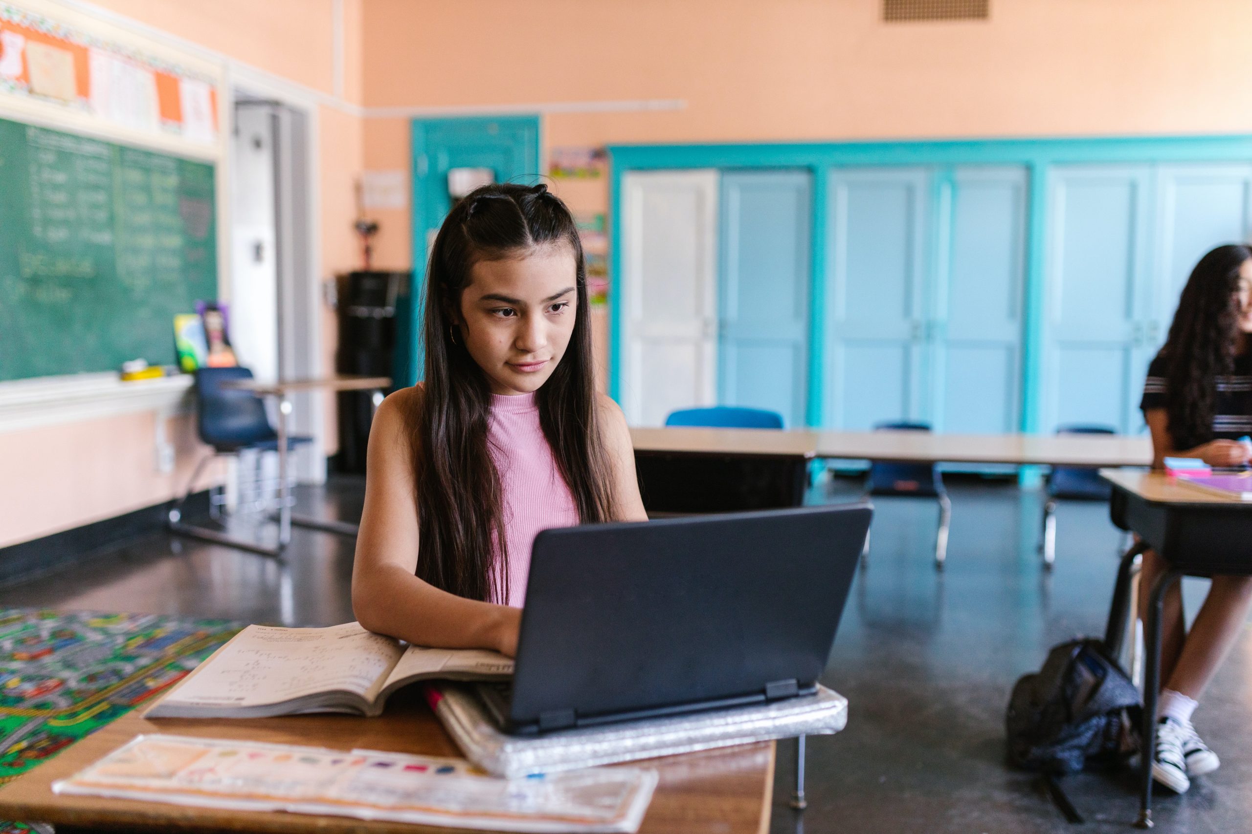 A Young Girl Typing on Her Laptop while Sitting on the Chair Inside the Classroom