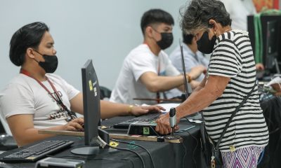 An elderly woman places her thumb on a scanning device for her biometric