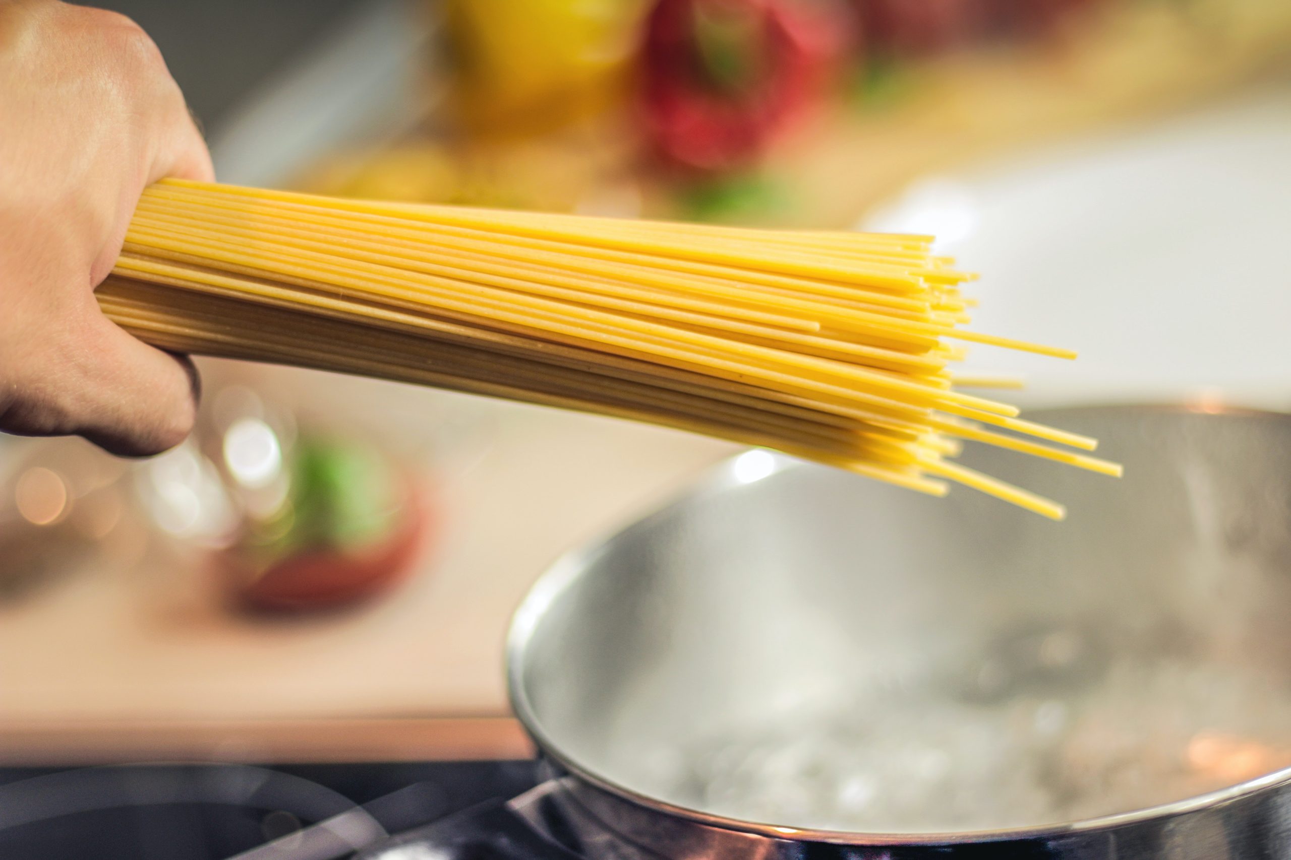 Person Holding Raw Pastas Aiming at Boiling Water in Pot