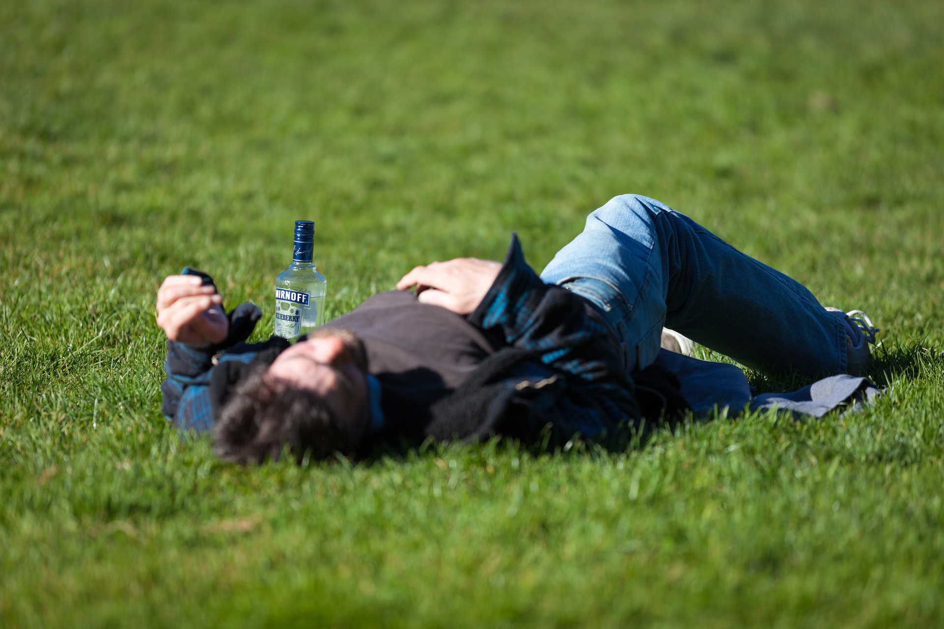 man laying on grass with alcohol bottle