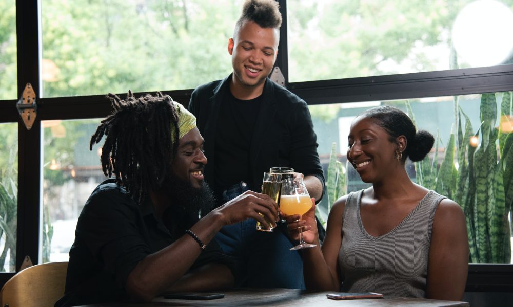 Three Persons Cheers With Clear Glasses Filled With Liquid Beverages Near Window