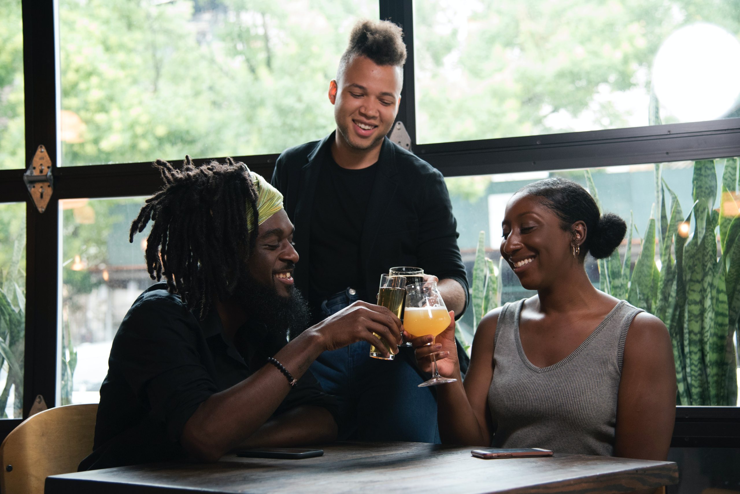 Three Persons Cheers With Clear Glasses Filled With Liquid Beverages Near Window