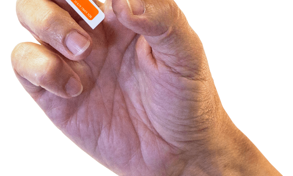 A hand holding a Kloxxado intranasal spray device. With the tip inserted into the nostril of someone who has suspected overdose, a dose of naloxone is administered by using one's thumb to push the plunger up toward the index and middle fingers.