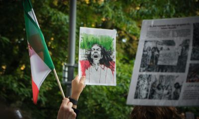 Hands Holding an Iranian Flag and a Protest Sign