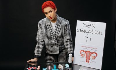 A Woman Wearing Formal Attire Standing Beside the Glass Table with Plastic Toys while Looking at the Camera