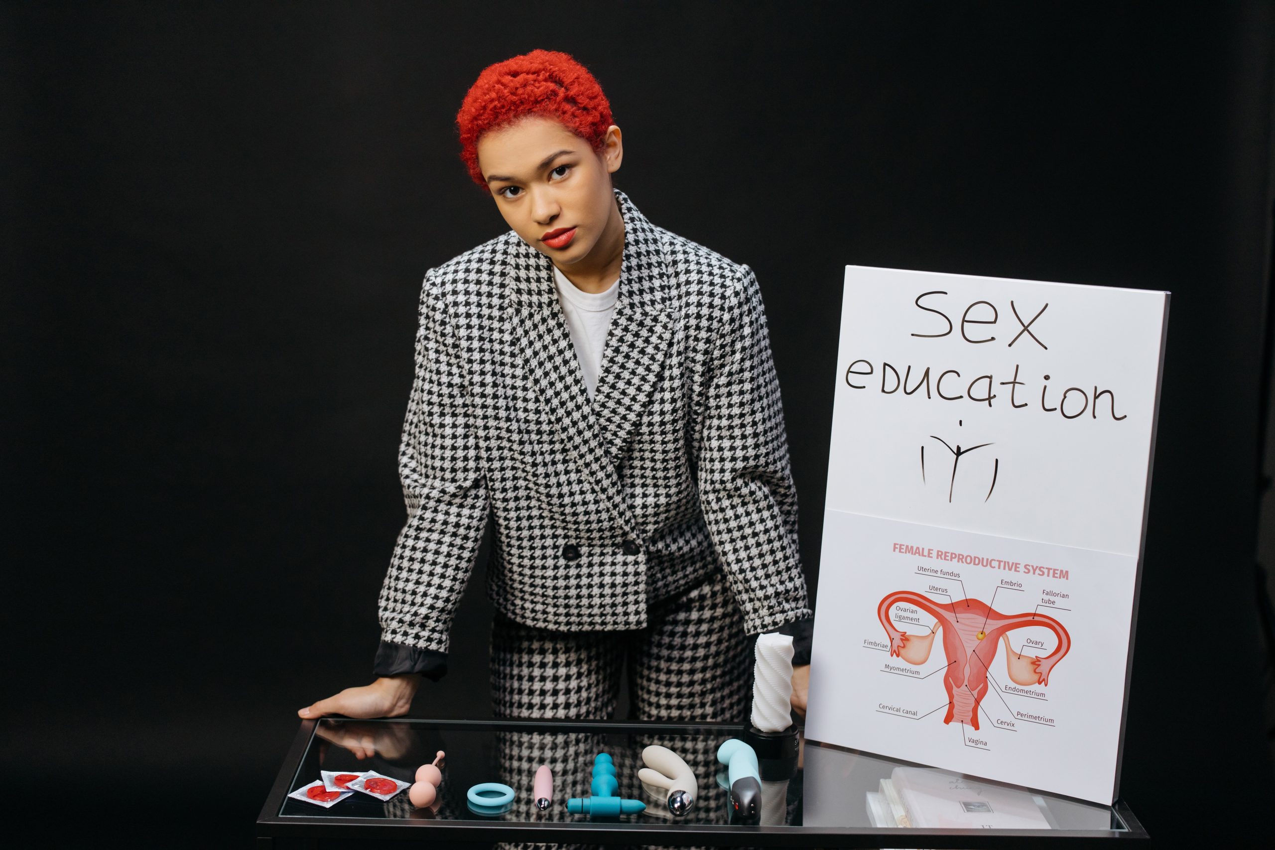 A Woman Wearing Formal Attire Standing Beside the Glass Table with Plastic Toys while Looking at the Camera