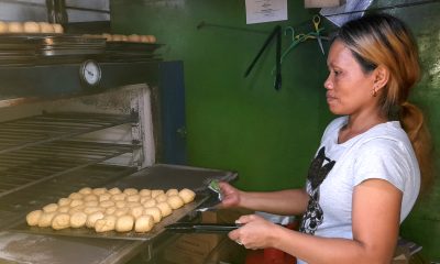 woman taking out a tray of pandesal from the oven