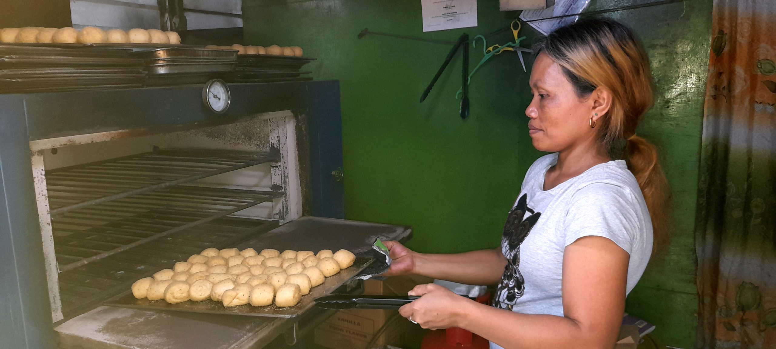 woman taking out a tray of pandesal from the oven
