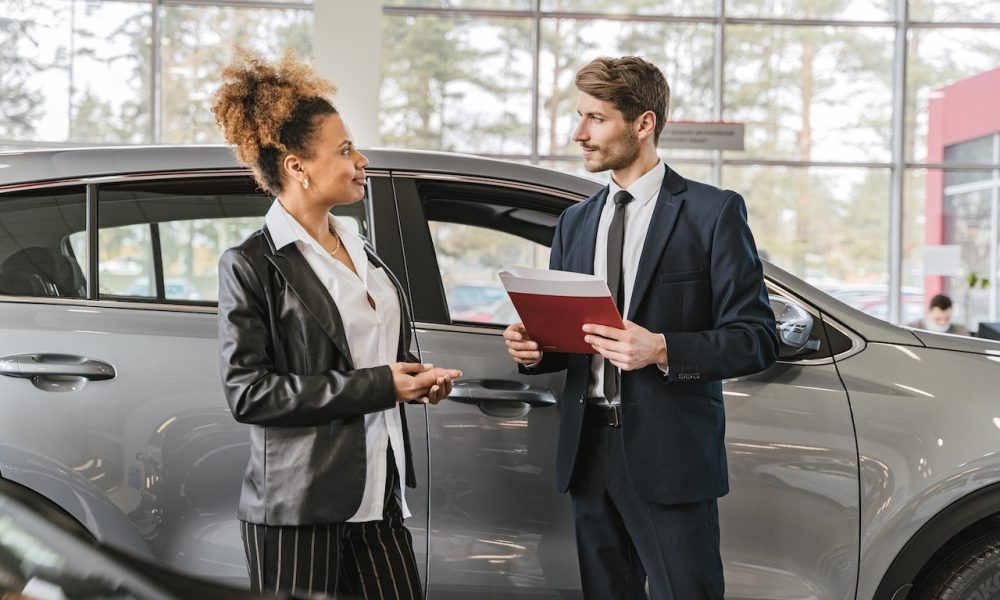 men and woman talking with folder and car behind